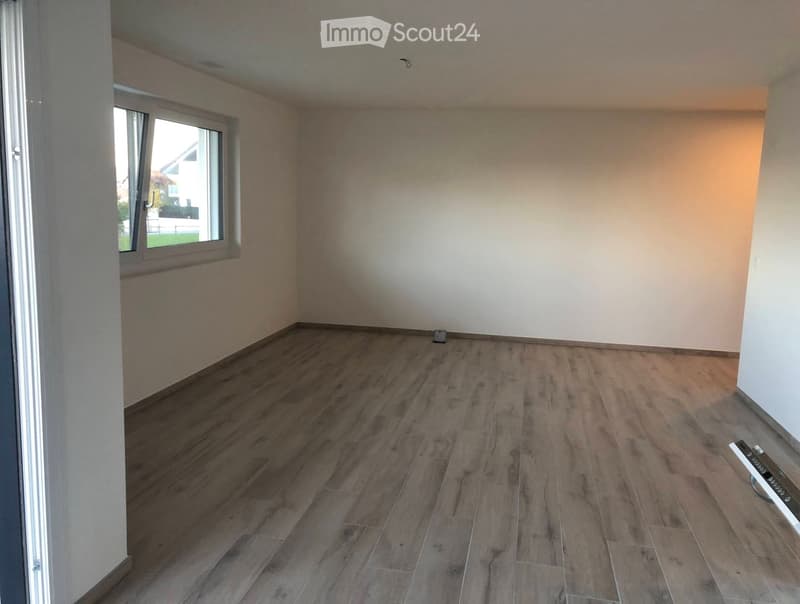 Empty room with wooden flooring and white walls, featuring a window with white frame and a door on the left side.