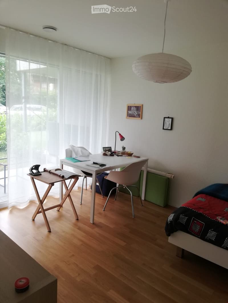 room with white desk, desk lamps, office chair, table with a stapler, bed with checkered blanket, windows with white curtains, ceiling lamp