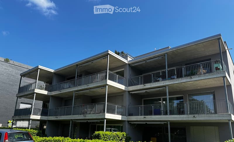 Modern 3-story apartment building with balconies, large windows, gray exterior, and enclosed entrance.