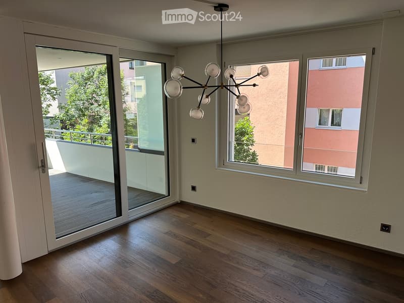 Empty room with wooden flooring, large windows, and a sliding glass door leading to a balcony.