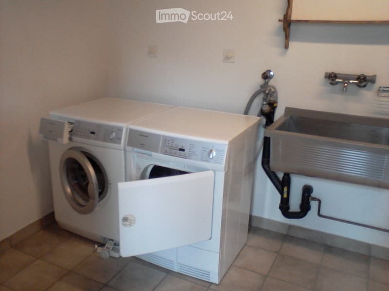 Bathroom with a washing machine, dryer, and sink. The washing machine door is open, and the sink is mounted on the wall with a faucet.