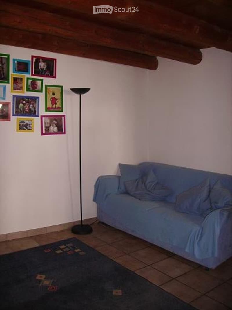 Living room with a blue sofa, floor lamp, and a small rug on a tiled floor. The walls are decorated with framed photos.