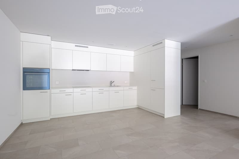Empty kitchen with white cabinets, stainless steel sink, and built-in oven. Light grey tiled floor and neutral-colored walls.
