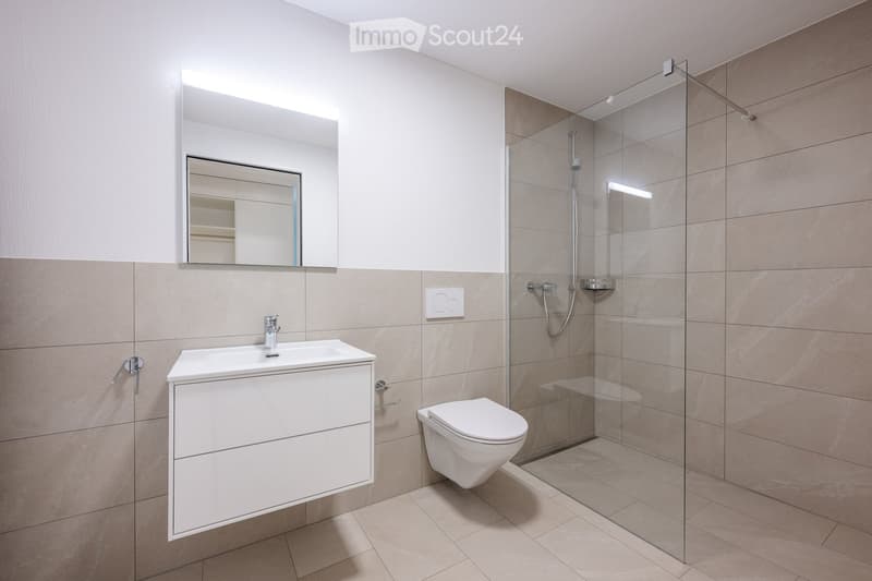 Modern bathroom with a white sink, mirror, toilet, and glass-enclosed shower. Beige tiles and sleek fixtures.