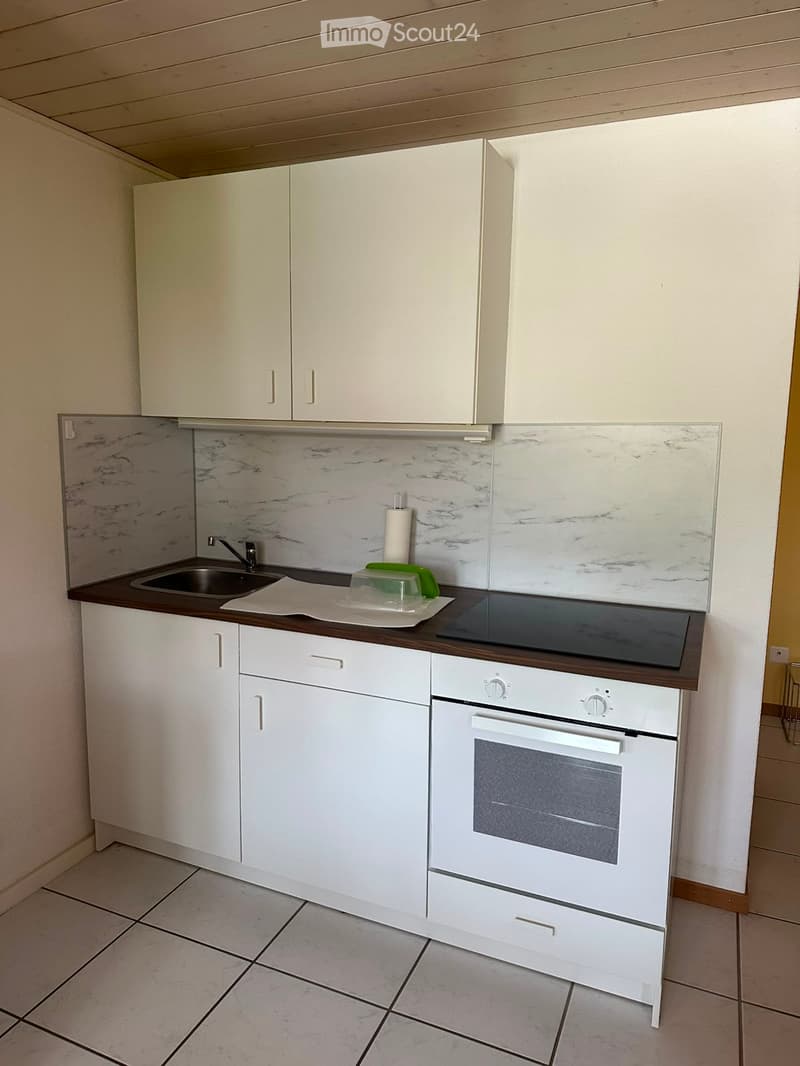 Modern kitchen with white cabinets, marble backsplash, and a dark wooden countertop. Features include a sink, faucet, induction cooktop, and built-in oven.