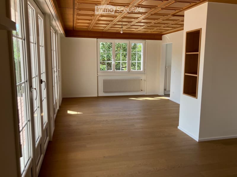 Empty room with wooden flooring, white walls, large windows, and built-in shelving unit.