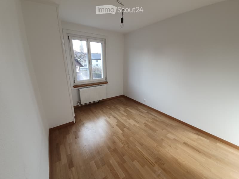 Empty room with wooden flooring, white walls, and a window with a radiator below it.