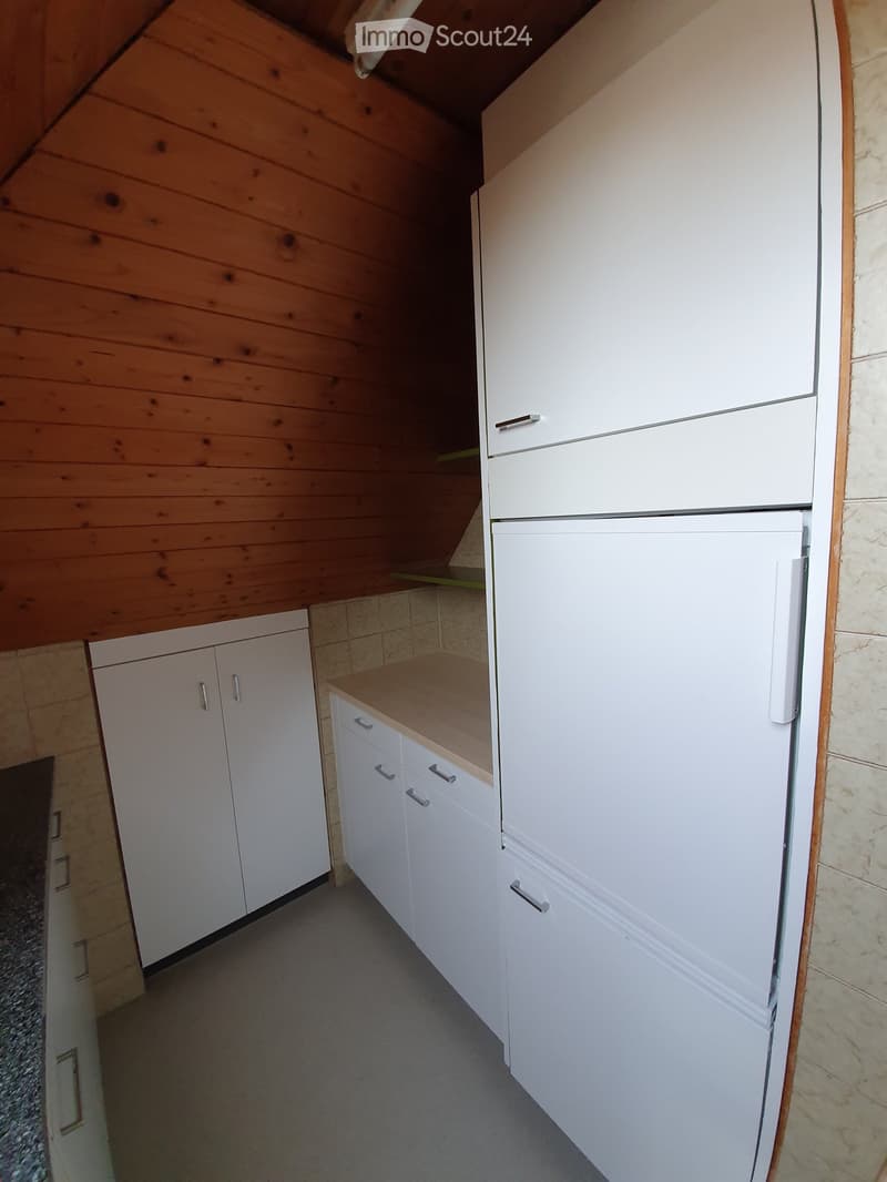 Modern kitchen with white cabinets, a refrigerator, and a countertop, featuring wooden walls and tiled flooring.