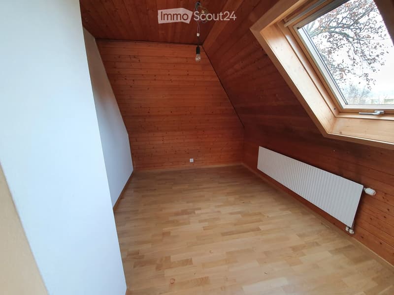 Empty attic room with wooden walls, ceiling, and floor, featuring a skylight window and a radiator on one wall.
