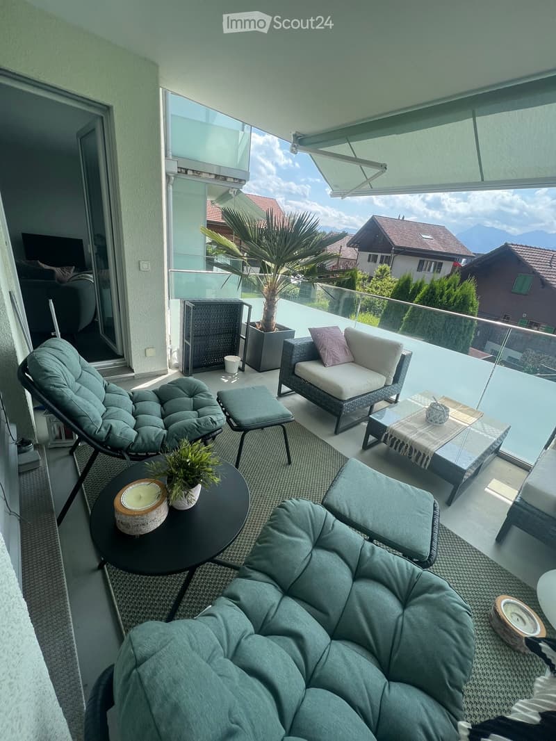 Balcony with modern furniture including a sofa, chairs, tables, and cushions, overlooking a scenic mountain view.