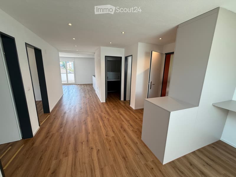 Empty hallway with wooden flooring, white walls, and several doors leading to different rooms.