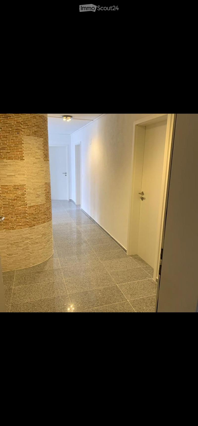 Empty hallway with tiled floor, beige walls, and a decorative brick column on the left side. Two doors are visible, one on each side of the hallway.