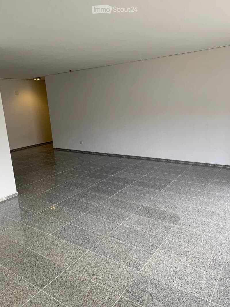 Empty room with grey tiled floor and white walls, featuring a small doorway on the left side.