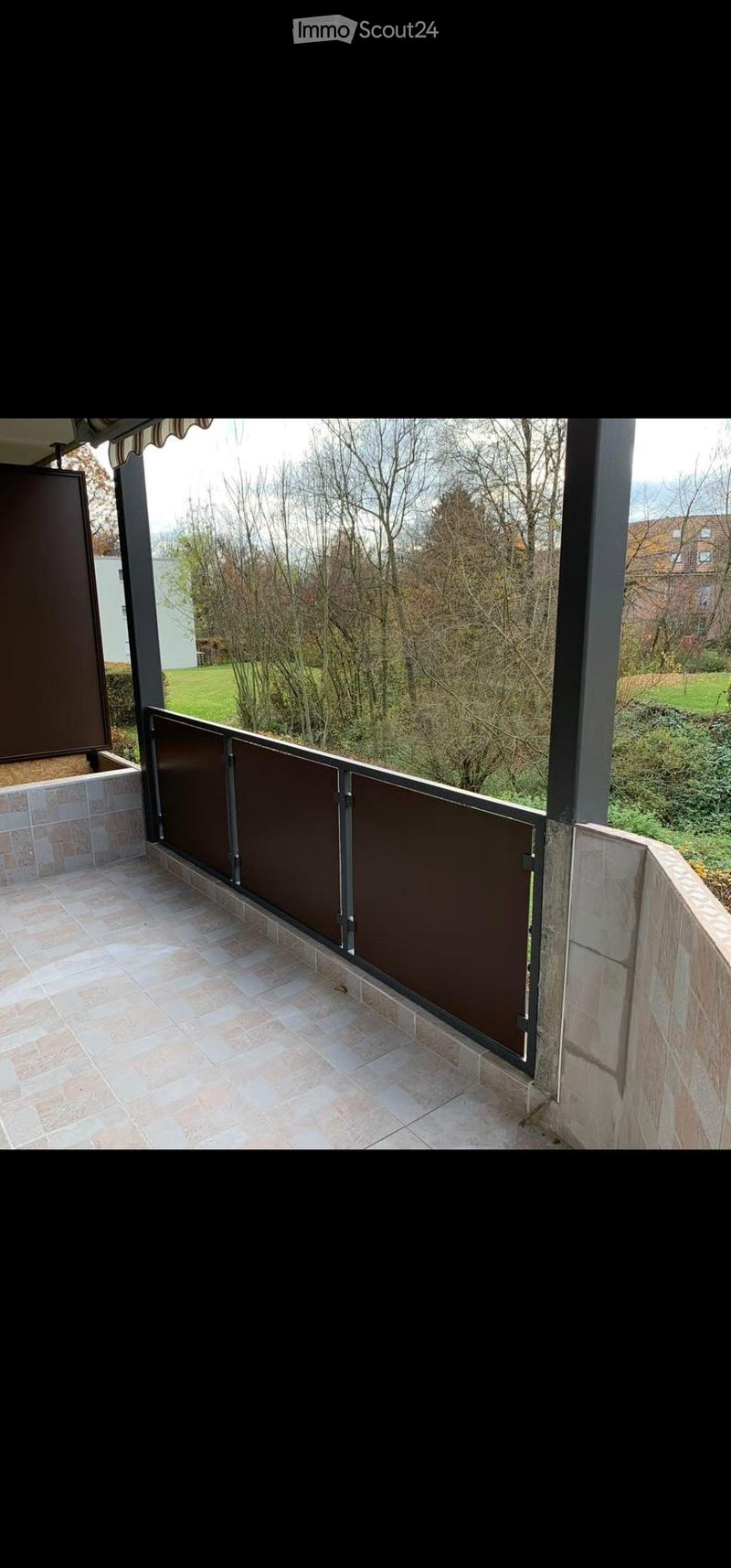 Balcony with tiled floor, metal railing, and view of a green landscape with trees and a house in the background.