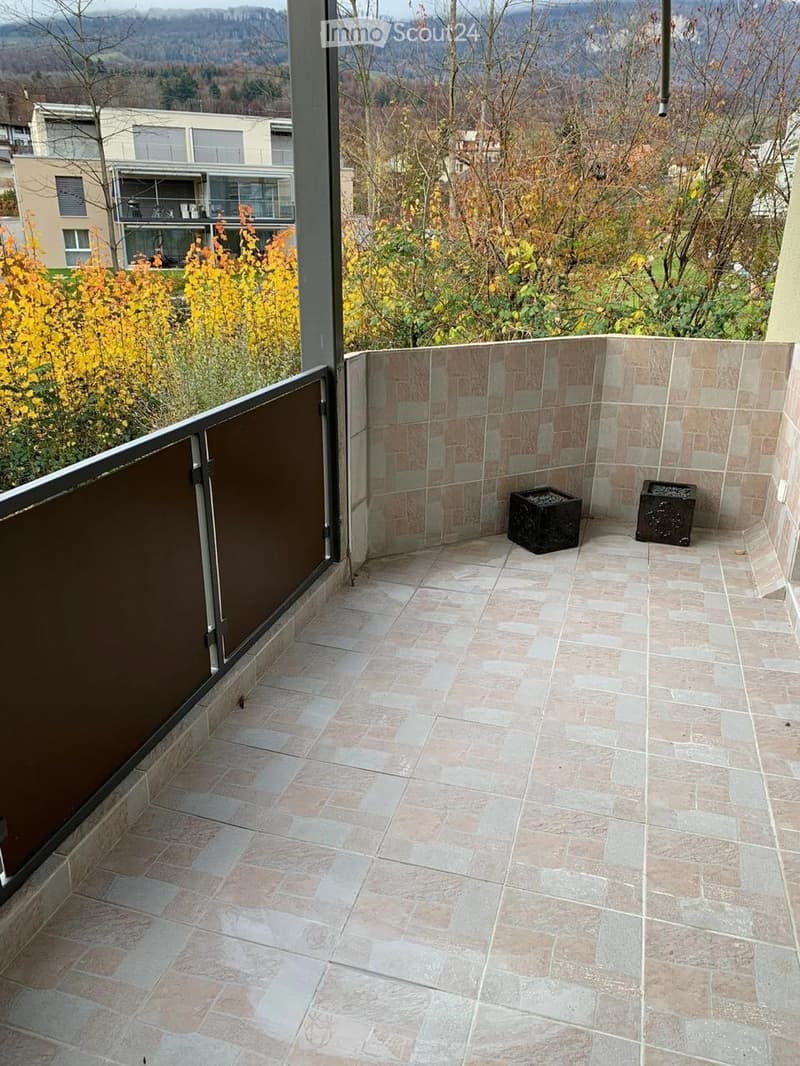 Balcony with tiled floor, low wall, and view of surrounding landscape and buildings.