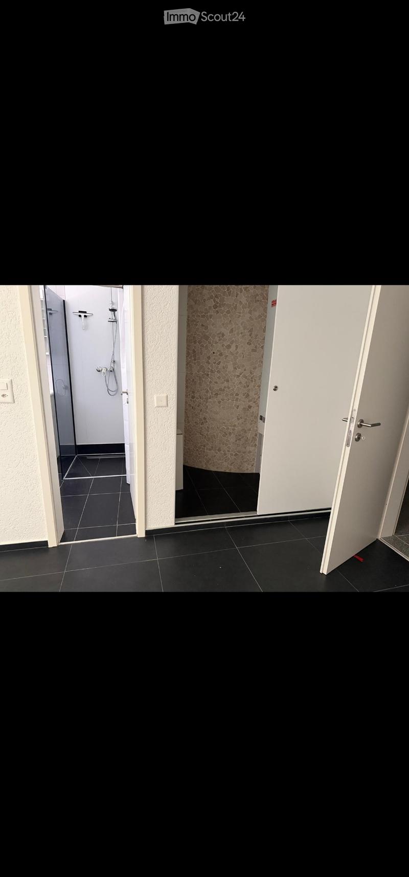 Empty hallway with black tiled floor, white walls, and two open doors leading to a bathroom and another room.