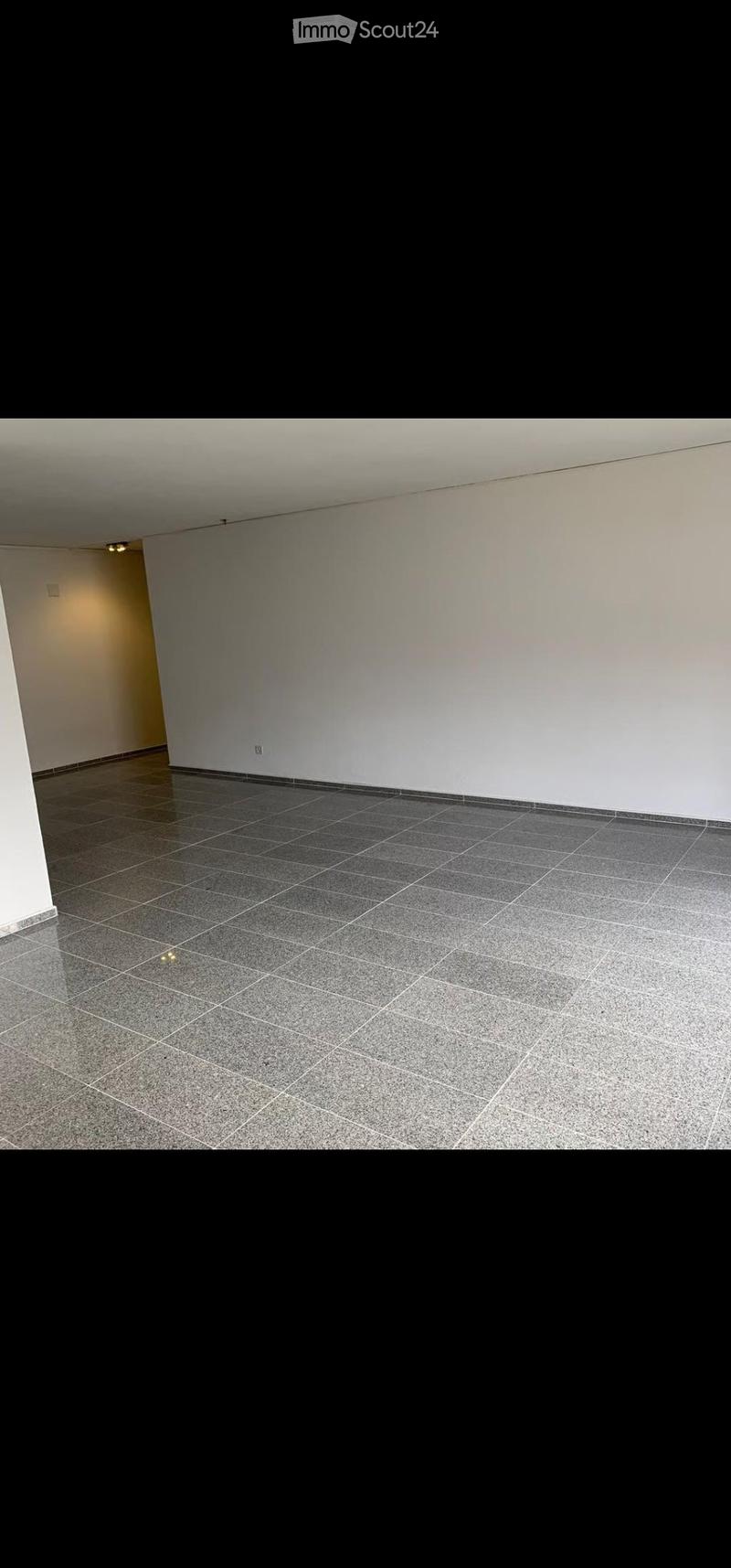 Empty room with grey tiled floor and white walls, featuring a small doorway on the left side.