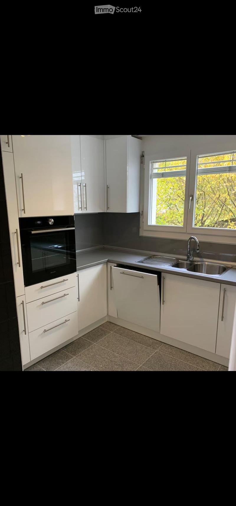 Modern kitchen with white cabinets, stainless steel sink, and built-in oven. Features a dark backsplash and tiled floor.