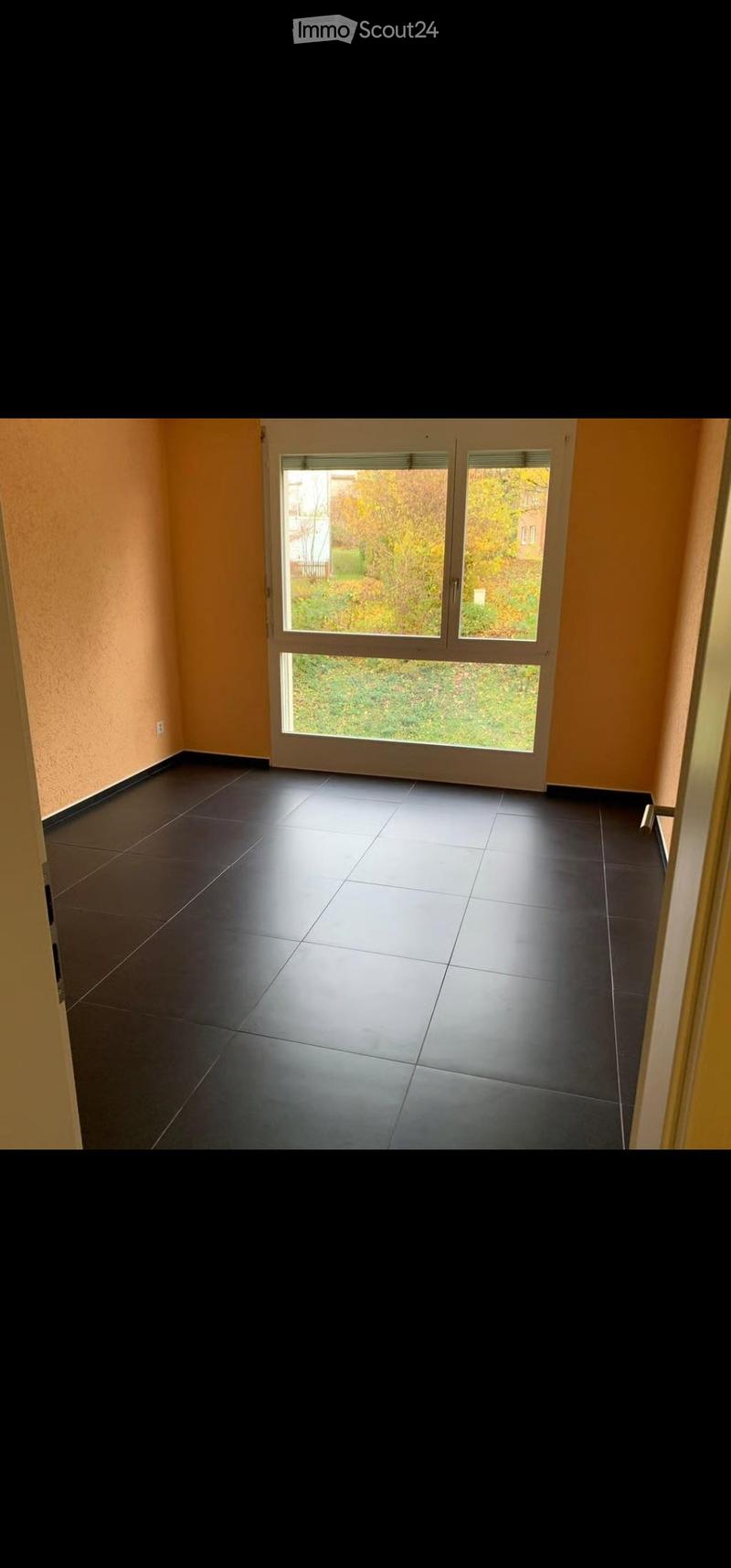 Empty room with dark tiled floor, light orange walls, and large sliding glass door leading to outdoor area.