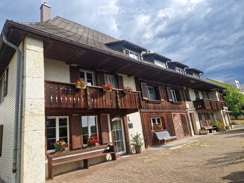 Two-story traditional house with wooden balconies, stone facade, and flower boxes on windowsills.