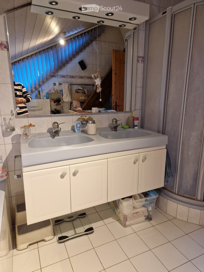 Bathroom with a double sink, white cabinets, mirror, toothbrush holder, and a basket on the floor.