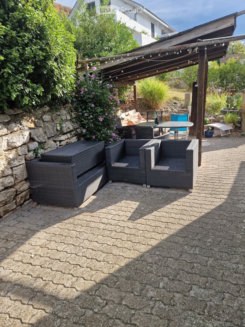 Outdoor patio with stone walls, wicker furniture, and a covered seating area with string lights.