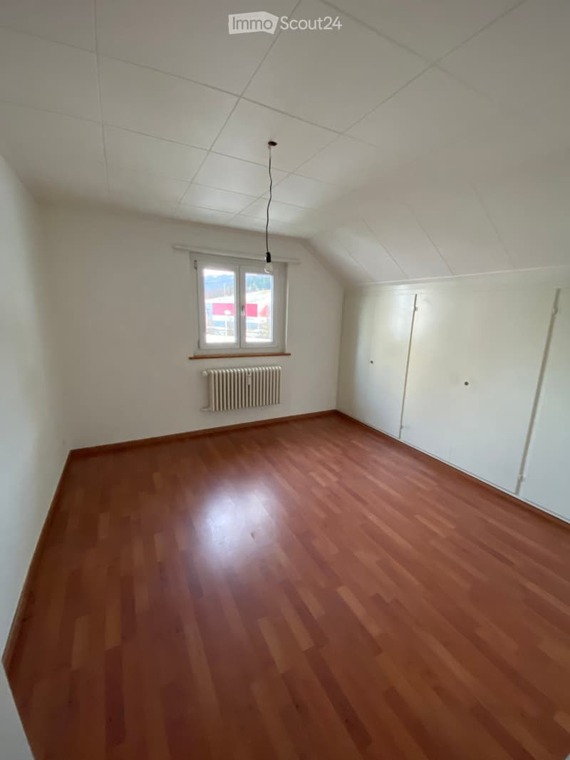 Empty room with wooden flooring, white walls, a window, a radiator, and built-in white closet units.