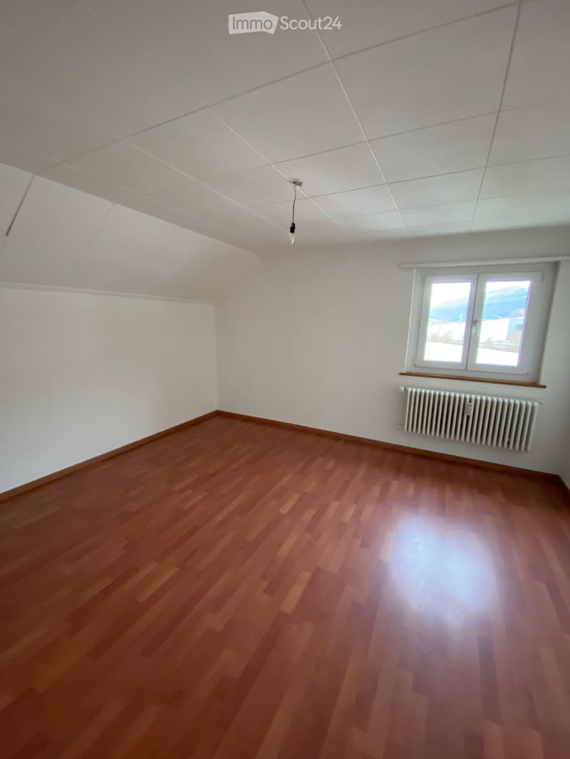 Empty room with wooden flooring, white walls, and a window with a radiator below it.