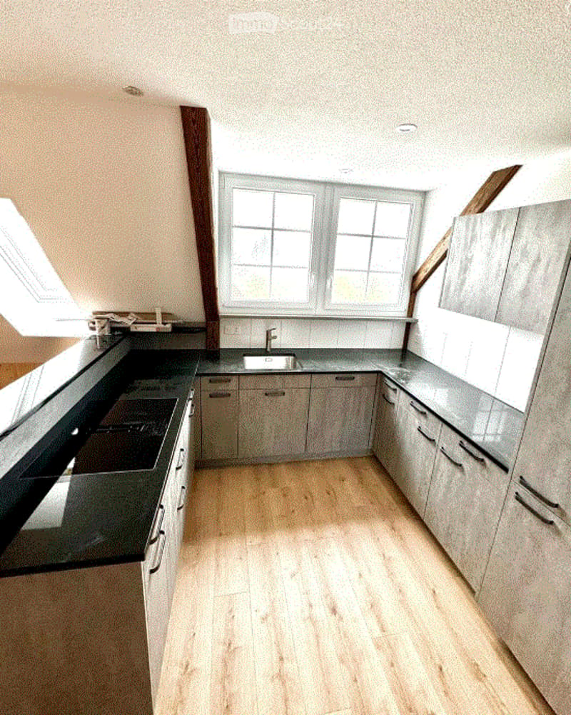Modern kitchen with light wooden flooring, grey cabinets, and a black countertop. Features a sink with a faucet and built-in storage cabinets.