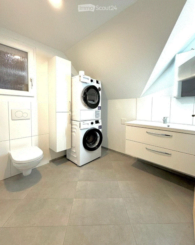 Modern bathroom with a toilet, washing machine, sink, and white cabinets.