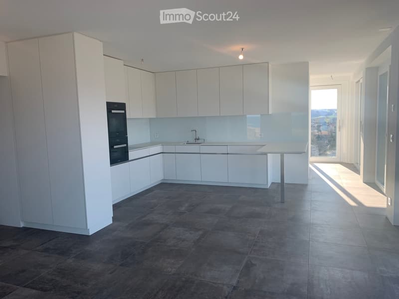 Modern kitchen with white cabinets, dark tiled floor, built-in oven, sink, and a small table.