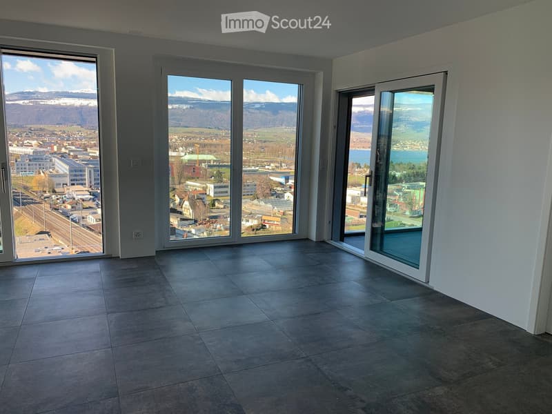 Empty room with large windows offering a scenic view of a cityscape and mountains, tiled floor, and white walls.