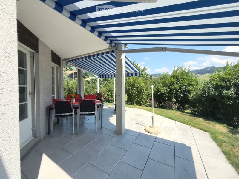 A covered patio with a blue and white striped awning, tiled floor, and outdoor dining set including a table and chairs.