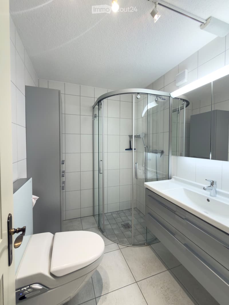 Modern bathroom with white tiles, a toilet, a sink with a modern faucet, a glass-enclosed shower, and built-in cabinets.