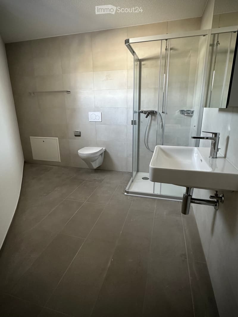 Modern bathroom with a toilet, sink, and glass-enclosed shower. Features tiled walls and floor, sleek fixtures, and a minimalist design.