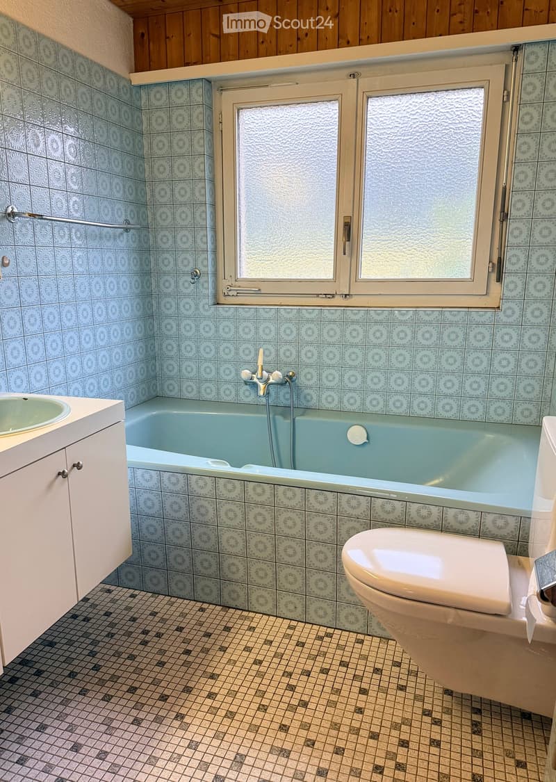 Bathroom with blue tiled walls, a bathtub, a toilet, a sink, and a window with frosted glass.