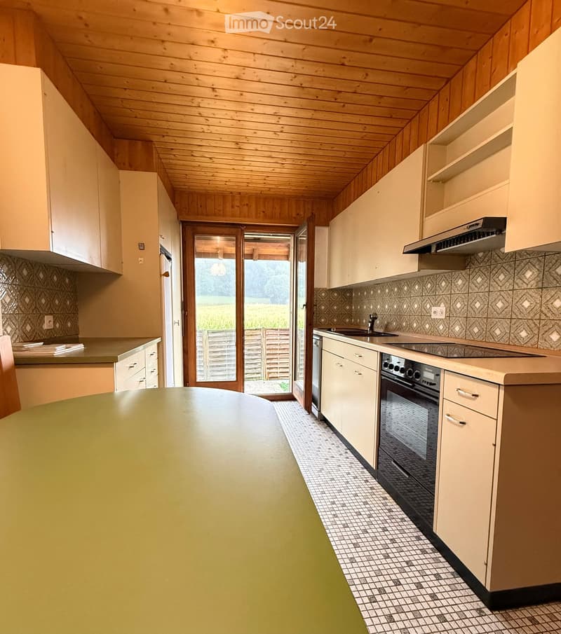 Bright kitchen with light-colored cabinets, a central island, and a view to the outdoors through a large glass door. The kitchen features a sink, stove, and range hood.