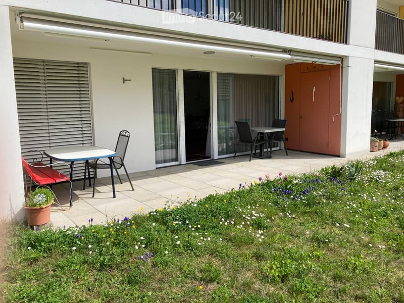 Balcony area with a small seating set, including a table and chairs, surrounded by a garden with flowers and plants.