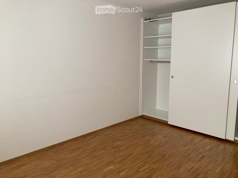 Empty room with wooden flooring and white walls, featuring an open closet with empty shelves.