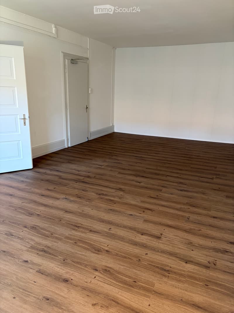 Empty room with wooden flooring, white walls, and two doors.