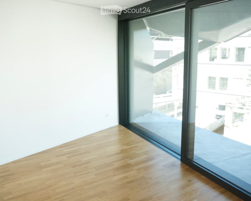 Empty room with light-colored wooden flooring and large glass sliding doors leading to a balcony or outdoor area.
