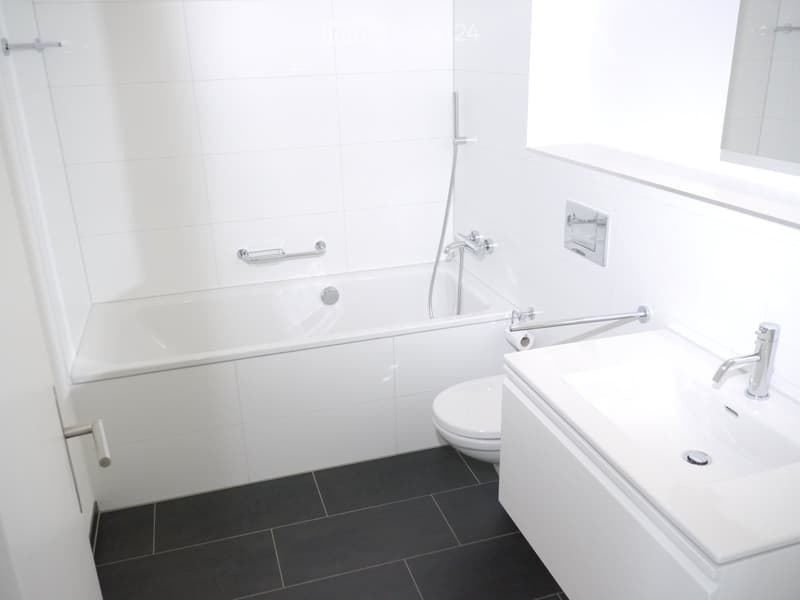 Modern bathroom with white tiles, a bathtub, a toilet, and a sink with a chrome faucet.