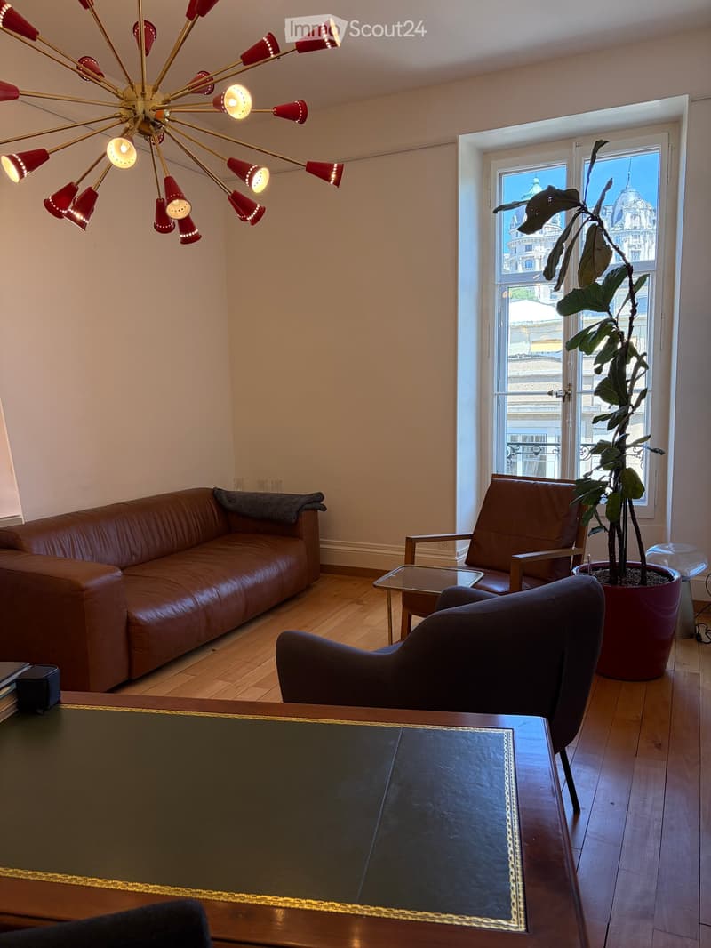Living room with a brown leather sofa, a dark green coffee table, a large decorative lamp, and a potted plant near the window.