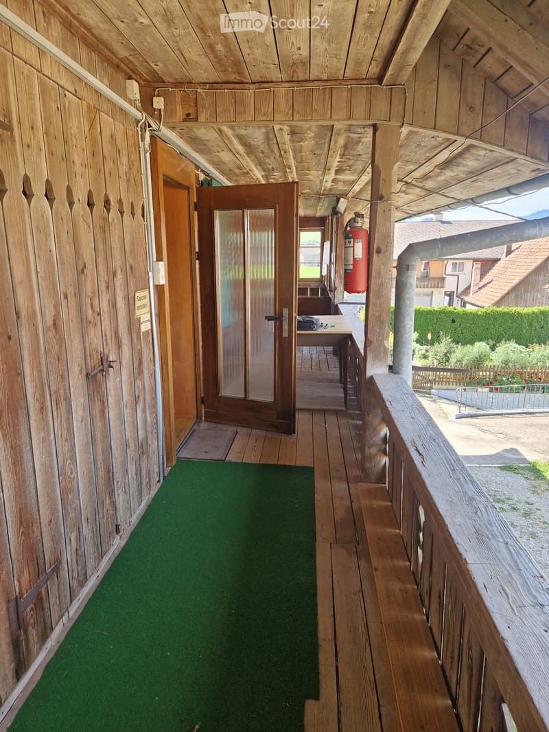 Wooden balcony with green artificial turf, wooden railing, and a door leading to an interior space.