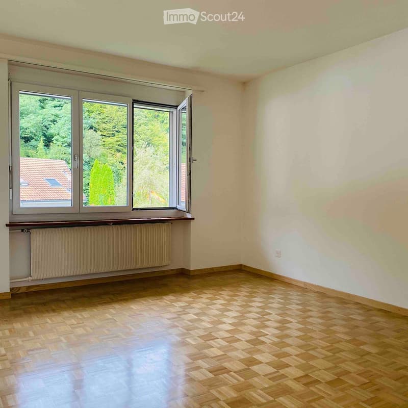 Empty room with wooden flooring, large windows, radiator, and white walls.