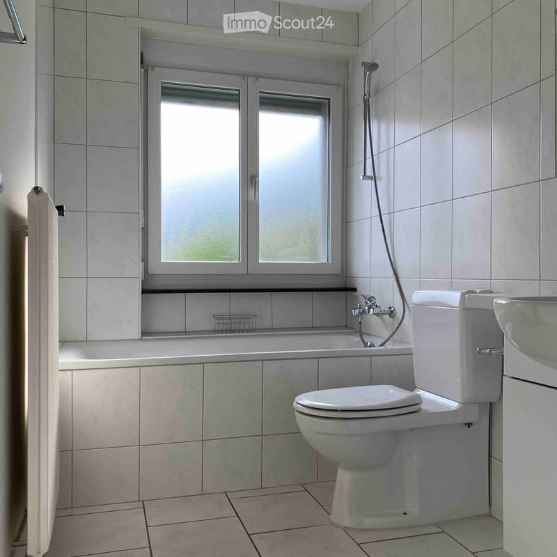 Modern bathroom with white tiles, a toilet, a sink, a bathtub, a showerhead, a mirror, and a towel on the side.