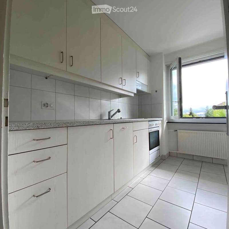 Modern kitchen with white cabinets, tiled backsplash, and a window overlooking a scenic view.