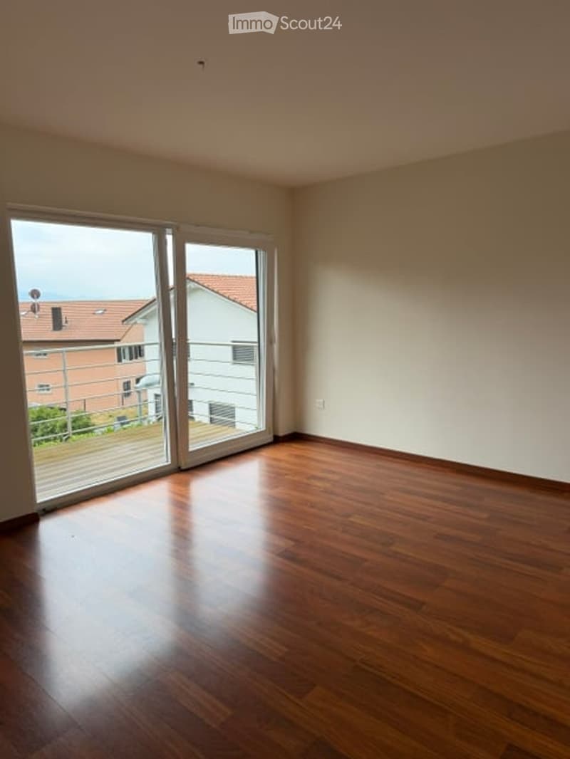 Empty room with wooden flooring and large sliding glass doors leading to a balcony.