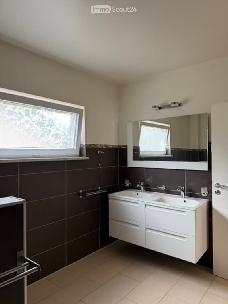 Modern bathroom with double sink, large mirror, dark brown tiles, and white cabinetry.