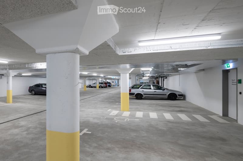 empty indoor parking lot with several yellow and white columns, well-lit, two cars parked, a lift is on the far right